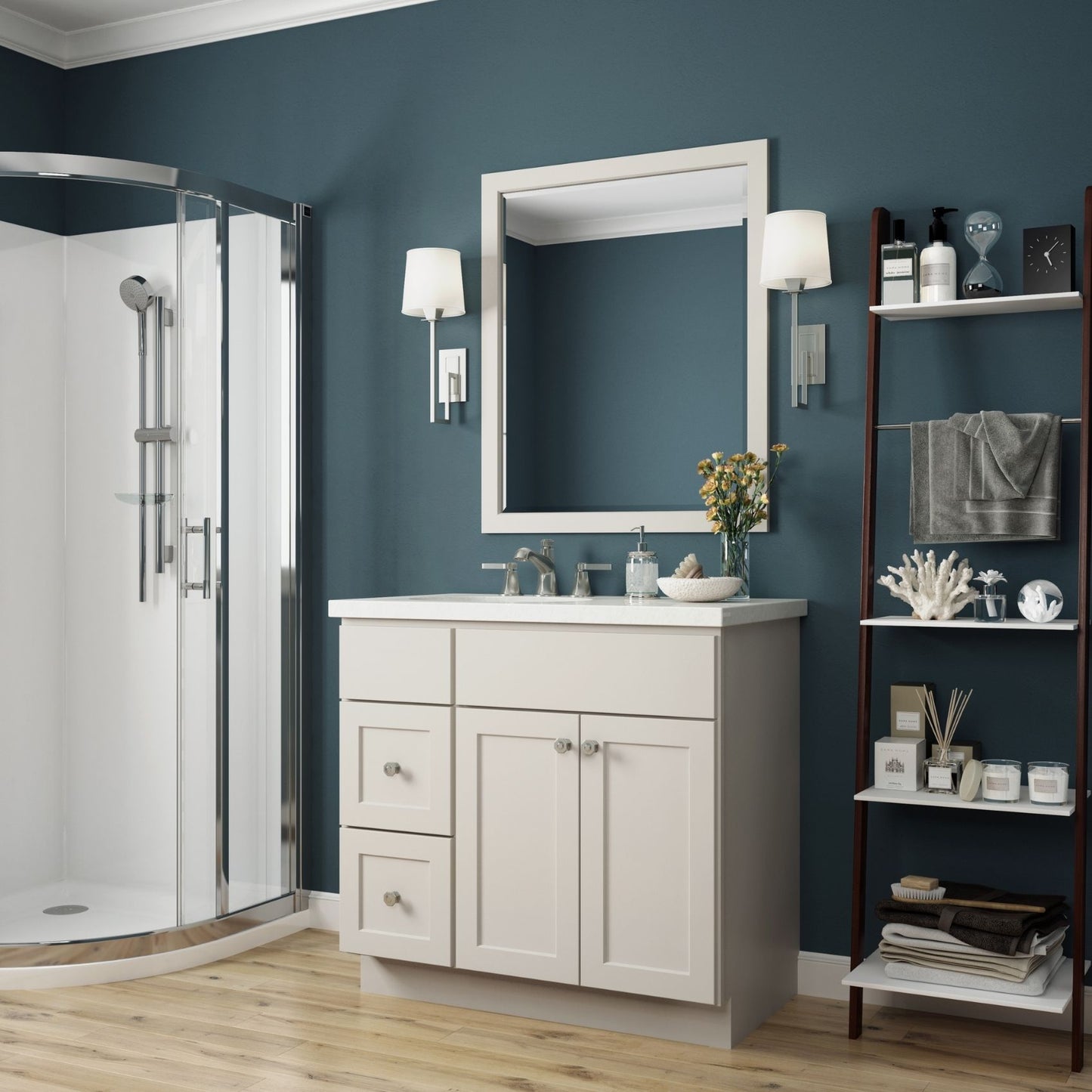 A bathroom vanity set featuring a white cabinet with silver knobs, a matching white rectangular mirror, and a white sink countertop, set against a dark blue wall. A glass shower enclosure is visible on the left, and a dark wood shelving unit stands on the right.