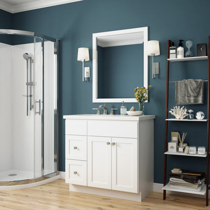 A white bathroom vanity cabinet with a white countertop and sink, shown in a styled bathroom setting with a blue wall, a glass shower enclosure, wall sconces, and a shelving unit.